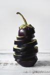 Purple Eggplant sliced and stacked back together on a white background.