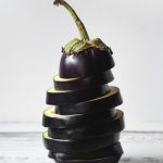 Purple Eggplant sliced and stacked back together on a white background.